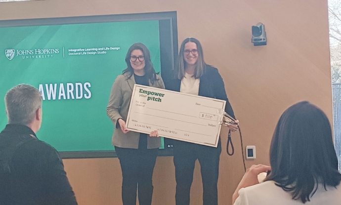 Two women stand on stage holding a giant check